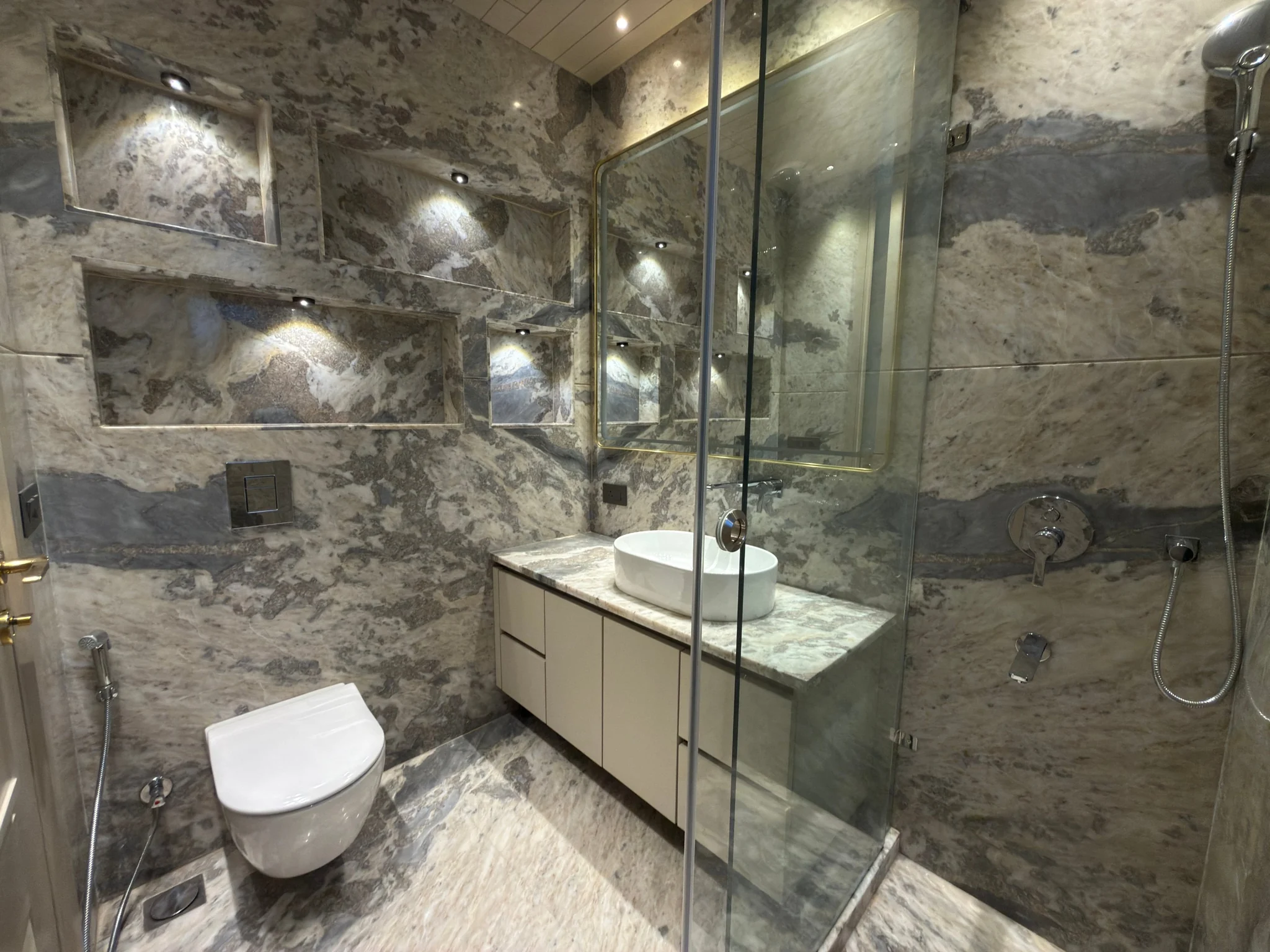 A bathroom in grey and white stone, with lit niches