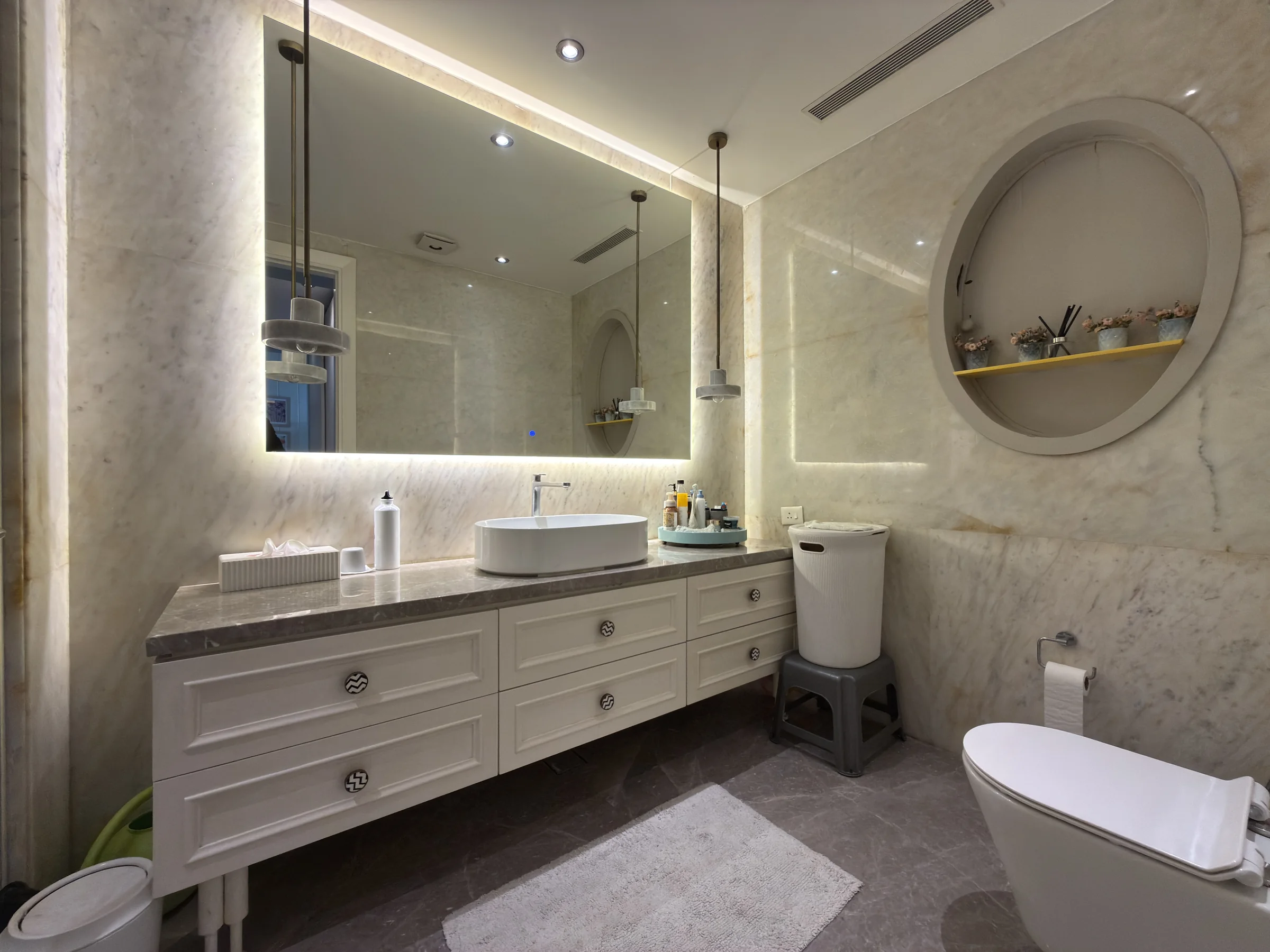 A bathroom in light stone, with a lit mirror