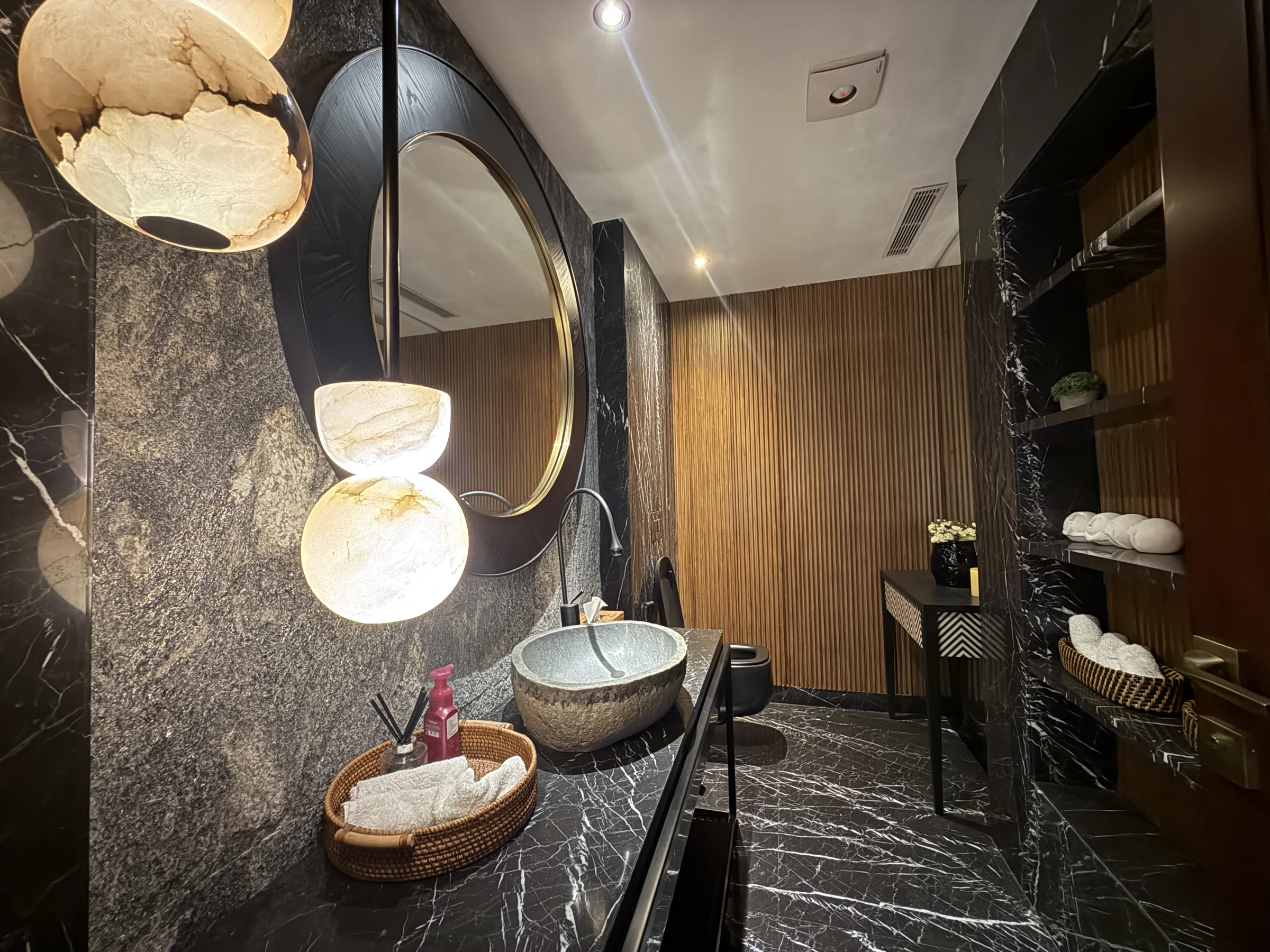 A washroom in dark stone, with a round mirror